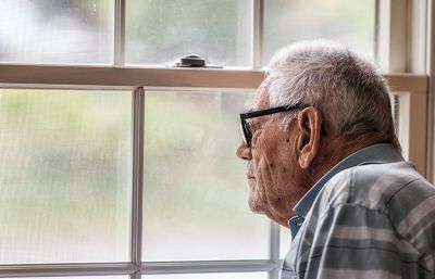 Elderly man looking through a window on a dark day