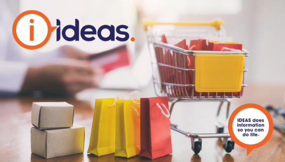 A miniature shopping trolley filled with packages. Shopping bags lay next to it.