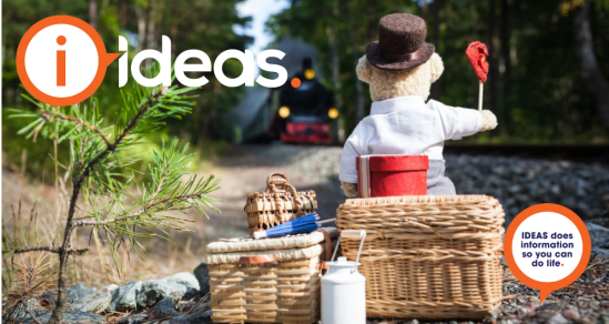 Concept photo of travel. A teddy bear sits on top of woven baskets signalling a steam train to stop. He has a hat box, pail and umbrella.