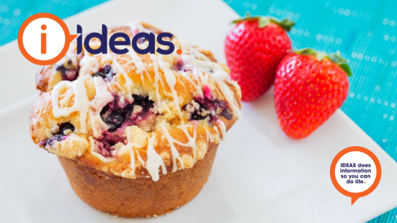 A bluberry muffin drizzled with white icing and two strawberries, all on a plate.