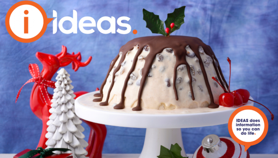 An ice-cream Christmas Pudding, on a plate with chocolate drizzles over the top. Christmas decorations are in the background.