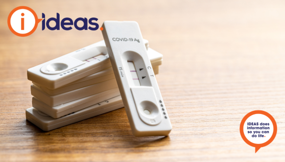 A pile of COVID-19 RAT tests on a table.