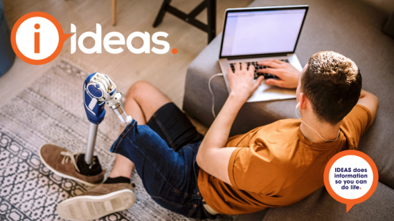 A young man with prosthetic leg is reclining on the floor and watching a laptop, he has earphones in. 