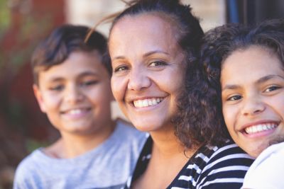 Image of smiling Aboriginal woman with two kids on either side of her.