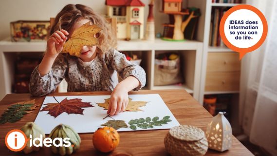 curly haired girl arranges leaves on a sheet of paper