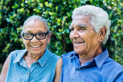 Image of smiling elderly Indigenous couple wearing blue shirts.