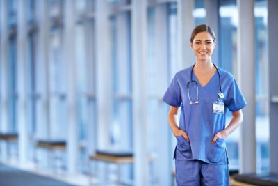 Image of smiling female nurse in blue nurse outfit standing in a hallway.