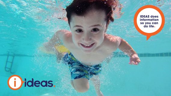 little boy swimming underwater in a pool. He is wearing swimming shorts.