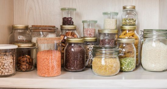 An image of a pantry shelf. Items like beans, nuts, lentils, rice, and pasta are stored in glass jars.