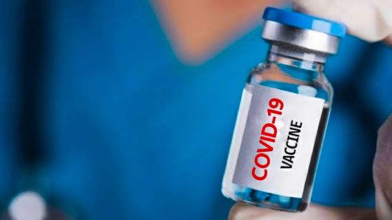  A medical professional is holding a small bottle between their fingers. The bottle is labelled COVID-19 Vaccine.