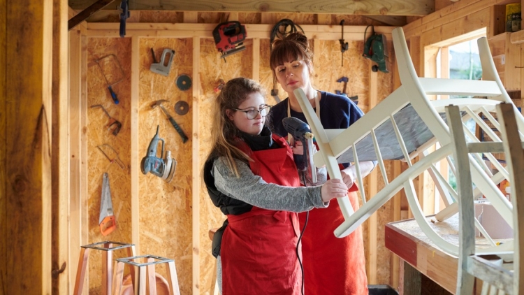 Girl with disability renovates a piece of furniture with help from another woman.