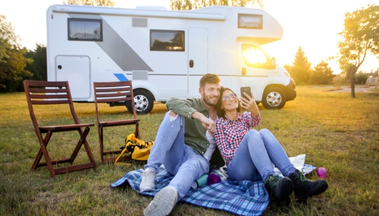 A couple on a picnic blanket in front of a motorhome. Sunset in the background.