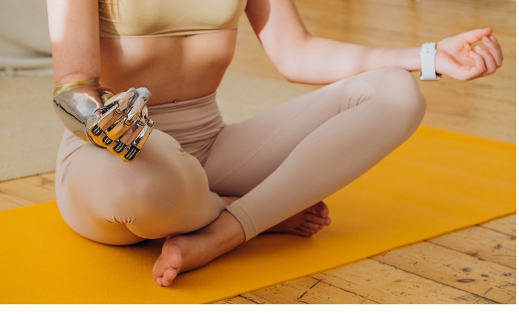 woman with metal prosthetic arm meditates on yellow mat