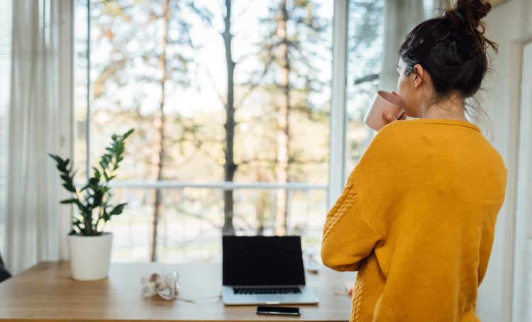 young woman taking a break, drinking from a mug and looking out the window