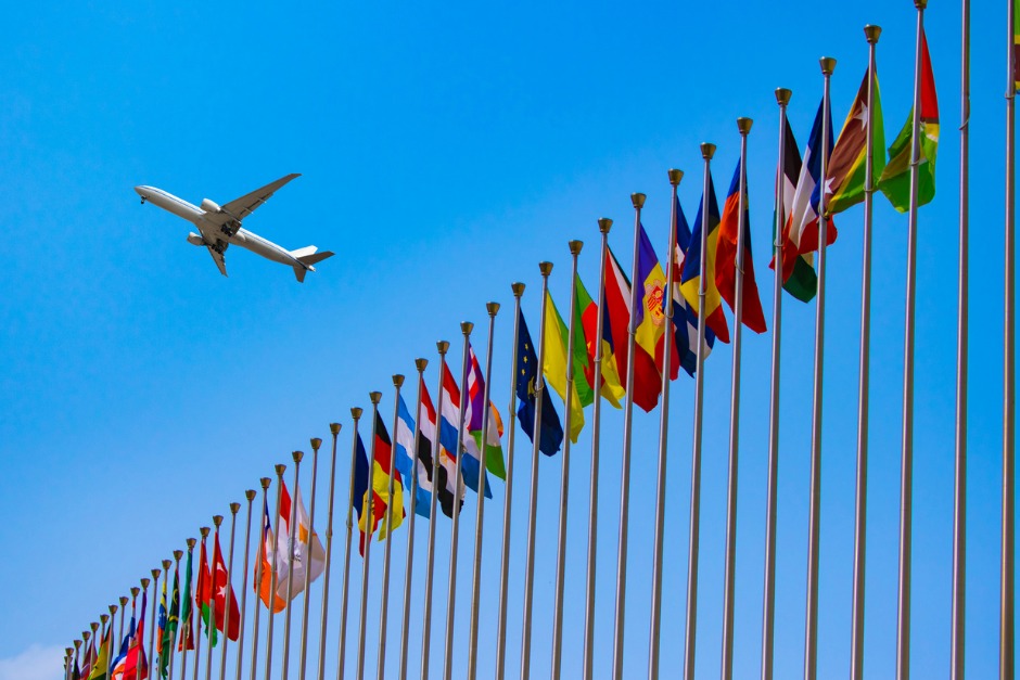 Image of aeroplane flying over row of International flags