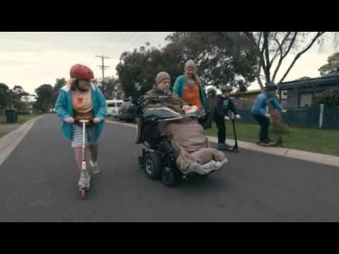 Man in wheelchair on the street with girl on a scooter