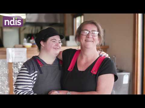 Victoria standing with a colleague arm in arm in the cafe that they work in.