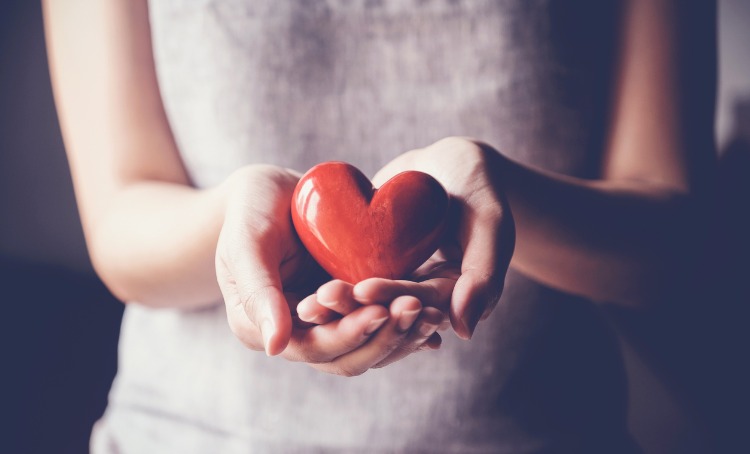 A woman cradles a ceramic red heart in her hands signifying support. A support concept photo.