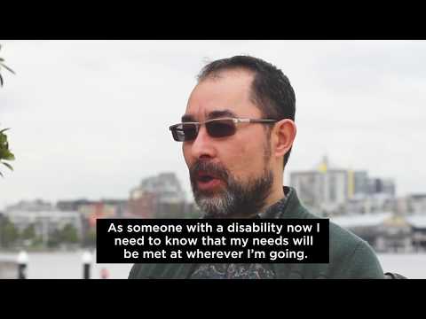 Man sitting in wheelchair with city and water backdrop speaking about travel and disability 