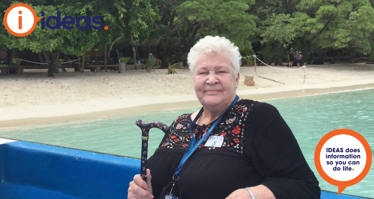 Mother in Law seated in a boat, with her cane, behind her is the shoreline.