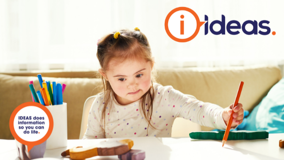 Young girl sitting at a table, drawing on a piece of paper with an orange pencil.