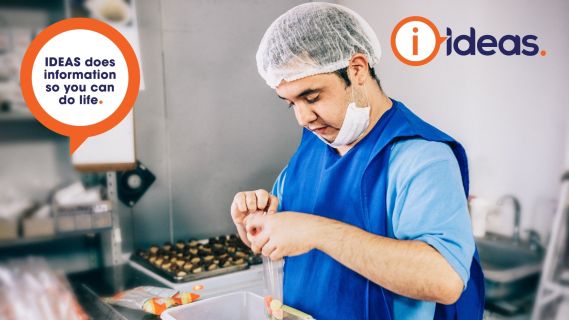 Young man with down syndrome wearing a hairnet, gloves and apron while peforming food handling tasks