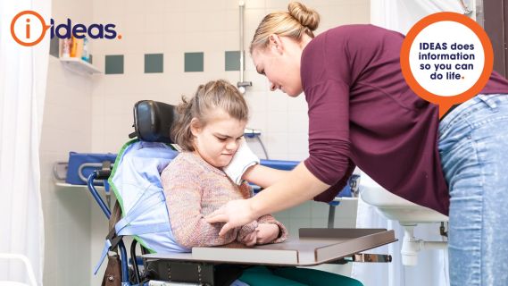 a careworker helping a young girl in a seated position in an accessible home bathroom