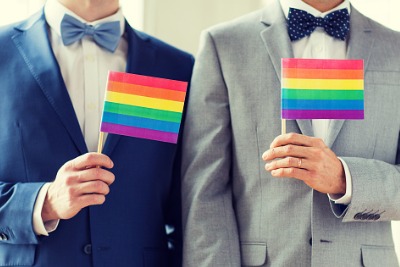 Detail of two men wearing suits and bow ties and holding rainbow coloured flags