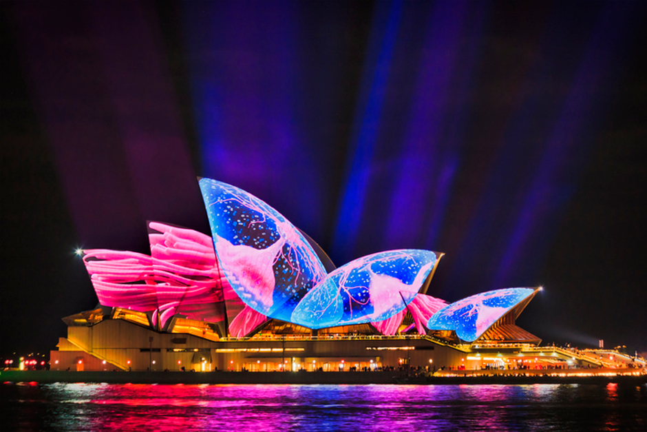 Image of the sails of the Sydney Opera House illuminated in electric blues and pinks.