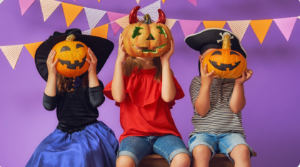 Image of 3 children dressed up as a witch, a devil and a pirate. All 3 are holding a pumkin in front of their faces.