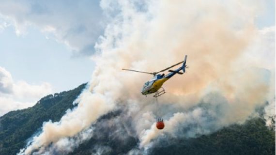 Image of a helicopter carrying a bucket of water near a bushfire.