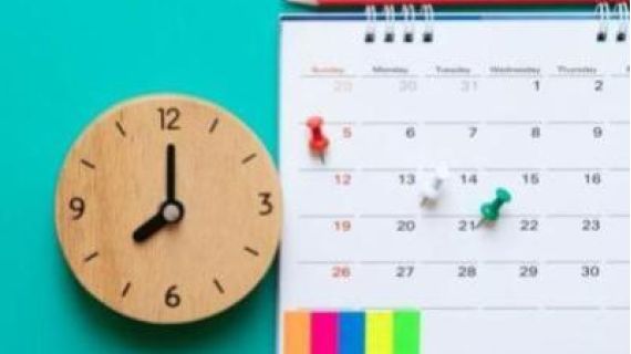 A close up a wooden clock and a calendar with pins and post-it notes.