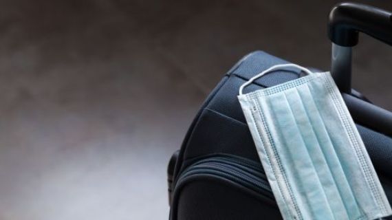 An image of a suitcase with a face mask sitting on top.