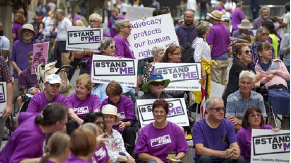 Image of people protesting in purple shirts with placcards