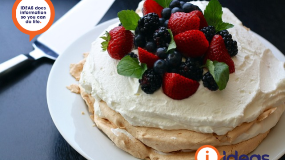 Pavlova dessert that has cream and mixed berries on top, sitting on a plate with a serving knife on the left.