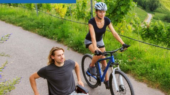 Man in a wheelchair on a path with a woman riding a pushbike beside him