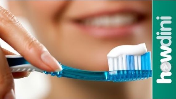 Toothbrush with toothpaste on it with a smiling lady behind it