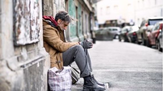 Image of homeless man sitting on a the side of a footpath.