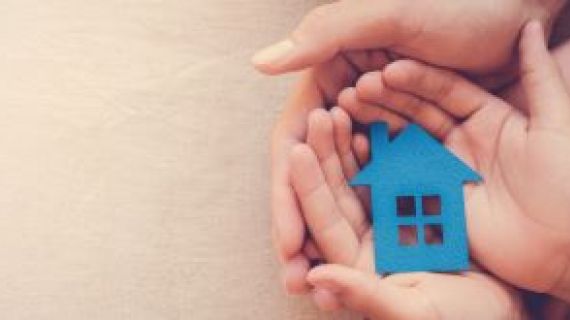 Adult hand cupping a child's hand holding a blue cutout paper house.