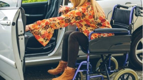 Young woman in a wheelchair getting in a car