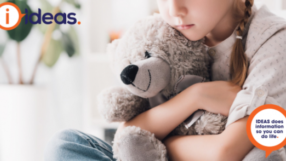 A young girl with a plait in her hair and a thoughtful look on her face is hugging a teddy bear. The teddy is smiling.