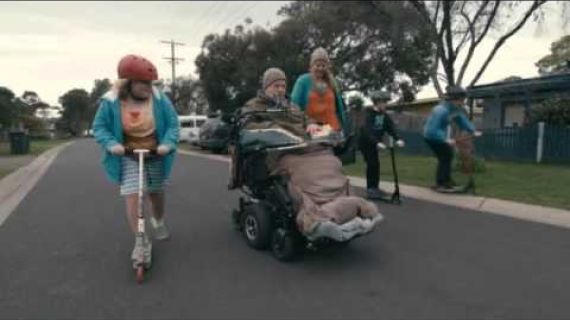 Man in wheelchair on the street with girl on a scooter