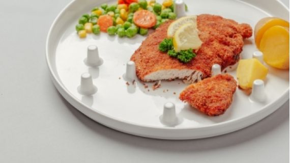 a white plate with crumbed chicken, peas and carrots and corn. the plate has white pegs and slight gradient.