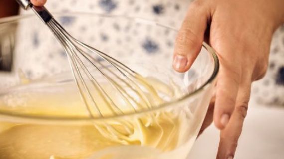 Image of a womans hands, holding a whisk, mixing a batter in a bowl.