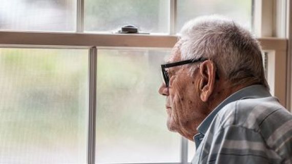Elderly man looking through a window on a dark day