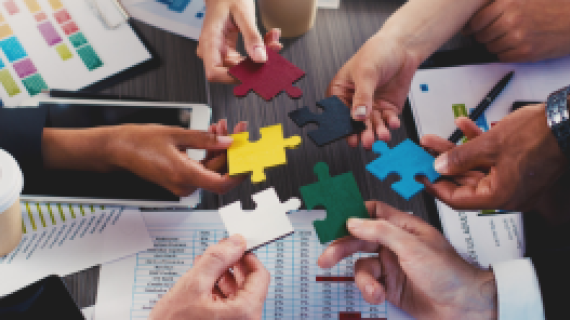 A diverse group of people holding different coloured puzzle pieces in a circle,