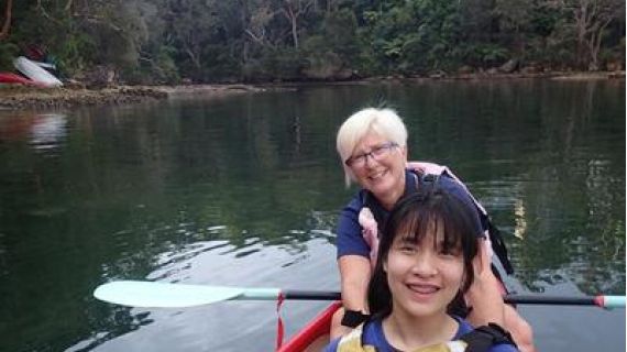 Two women sitting in a boat. Both are smiling and one is holding an oar.
