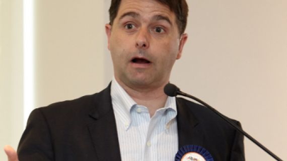 Image of Alastair McEwin speaking and wearing a blue show ribbon labelled "Headliner"