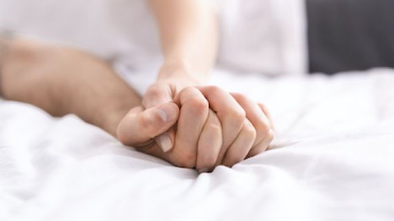 detail of couple's hands clasped tightly on a bed
