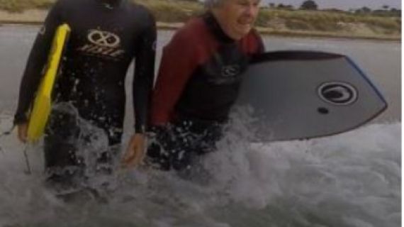 Two people walking into the ocean with boogie boards